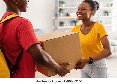 Delivery Concept. Happy African American Woman Receiving Big Box From Courier Man In Red Uniform Standing At Doors Of Her Home. Cropped Shot, Selective Focus On Paperboard Parcel. - Powered by Shutterstock