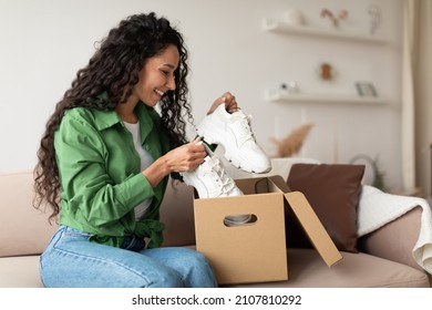 Delivery Concept. Happy Female Buyer Holding Footwear Unpacking Cardboard Box Sitting On Couch At Home. Joyful Customer Woman Receiving Shoes After Successful Online Shopping