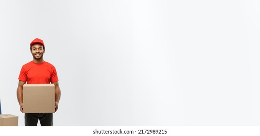 Delivery Concept - Portrait of Handsome African American delivery man or courier with hand truck and holding box. Isolated on Grey studio Background. Copy Space.