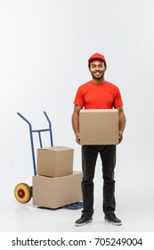 Delivery Concept - Portrait Of Handsome African American Delivery Man Or Courier With Hand Truck And Holding Box. Isolated On Grey Studio Background. Copy Space.