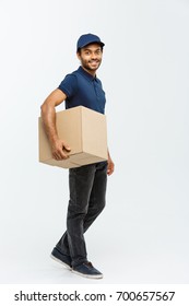 Delivery Concept - Portrait of Happy African American delivery man in blue cloth walking to send a box package to customer. Isolated on Grey studio Background. Copy Space.