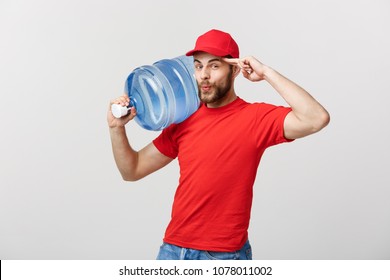 Delivery Concept: Portrait of smiling bottled water delivery courier in red t-shirt and cap carrying tank of fresh drink isolated over grey background