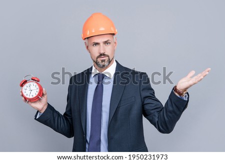 delivery of construction object on time. businessman in protective helmet. safety business workaholic behind schedule. architect hold alarm clock. first time home buyer. getting late. deadline.