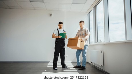 Delivery courier writing on clipboard checking inventory of cardboard box brought by client - Powered by Shutterstock