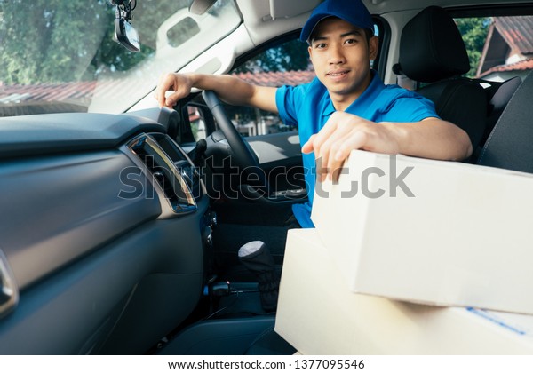 Delivery driver driving car with packages on\
seat outside the\
warehouse.