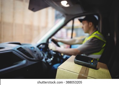 Delivery Driver Driving Van With Parcels On Seat Outside Warehouse