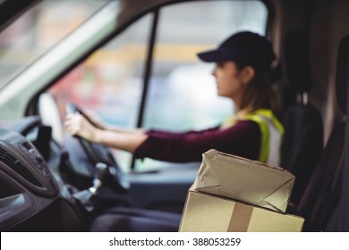 Delivery Driver Driving Van With Parcels On Seat Outside Warehouse