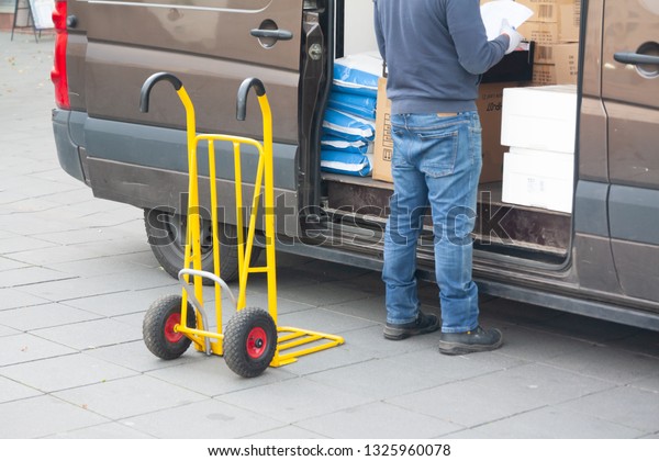 Delivery driver is unloading cargo van with goods\
to truck.