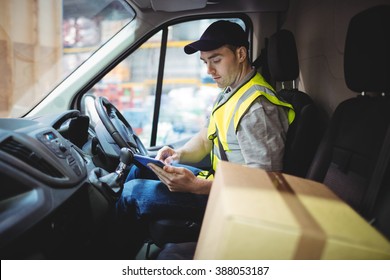 Delivery driver using tablet in van with parcels on seat outside warehouse - Powered by Shutterstock