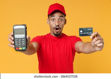 Delivery employee african man 20s in red cap t-shirt uniform work courier service hold wireless bank payment terminal to process and acquire credit card payments isolated on yellow background studio - Shutterstock ID 1864537558