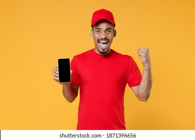Delivery employee african man in red cap blank print t-shirt uniform workwear work courier service concept hold in hand using mobile cell phone free space screen isolated on yellow background studio