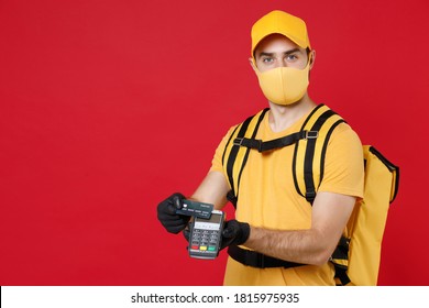 Delivery Employee Man In Yellow Cap Face Mask Gloves T-shirt Uniform Thermal Food Bag Backpack, Hold Bank Payment Terminal Work Courier Service During Covid-19 Virus Isolated On Red Background Studio