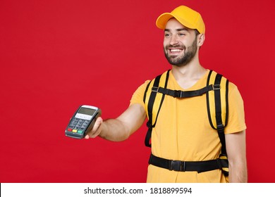 Delivery Employee Man In Yellow Cap T-shirt Uniform Thermal Food Bag Backpack Work Courier Service During Quarantine Coronavirus Covid-19 Virus Hold Bank Terminal Isolated On Red Background Studio.