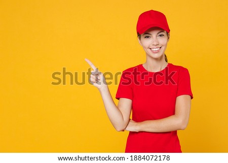 Delivery employee woman in red cap blank t-shirt uniform work courier in service during quarantine coronavirus covid-19 virus, pointing fingers aside on workspace isolated on yellow background studio