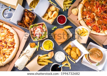 Delivery fastfood ordering food online concept. Large set of assorted take out foods pizza, french fries, fried chicken nuggets, burgers, salads, chicken wings, sides, black concrete background