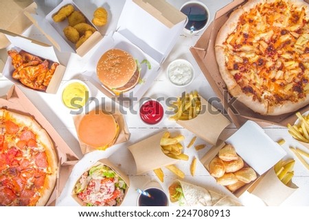 Delivery fastfood ordering food online concept. Large set of assorted take out foods pizza, french fries, fried chicken nuggets, burgers, salads, chicken wings, various sides, white table background 