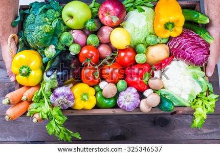 Delivery of fresh organic vegetables and fruits in wooden box, local market food.Hands holding box with vegetables and fruits background copy space.