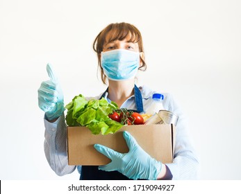 Delivery Girl Or Small Shop Owner In Blue Apron With Protective Face Mask Holding Food Delivery Box With Gloved Hands. Safe Delivery, Grocery Shopping Concept