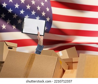 Delivery of goods to USA . Mans hand among cardboard boxes. Clipboard and USA flag. Concept of delivery by American regions. Hand of storekeeper among parcels. USA Delivery business. Copy space