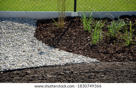 delivery of gray river pebbles like mulch to flower beds in the garden using a wheelbarow from the body of a truck or trailer. shovel and rake the layer over the black nonwoven fabric.