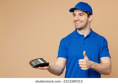 Delivery guy employee man wear blue cap t-shirt uniform work as dealer courier hold wireless modern bank payment terminal process acquire credit card show thumb up isolated on plain beige background - Powered by Shutterstock