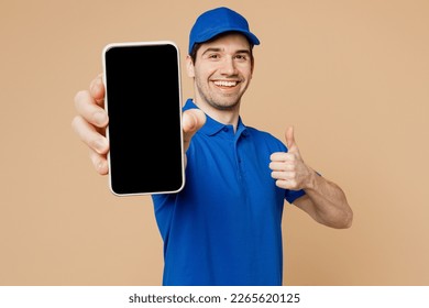 Delivery guy employee man wearing blue cap t-shirt uniform workwear work as dealer courier hold in hand use mobile cell phone with blank screen area show thumb up isolated on plain beige background - Shutterstock ID 2265620125