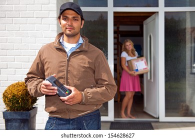 Delivery guy, holding a wireless pin machine walking away from a house, where a woman stands in the doorway, with the just delivered parcel in her hand
