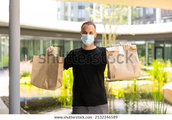 Delivery guy with protective mask\
and gloves holding bag with groceries in front of a\
building.