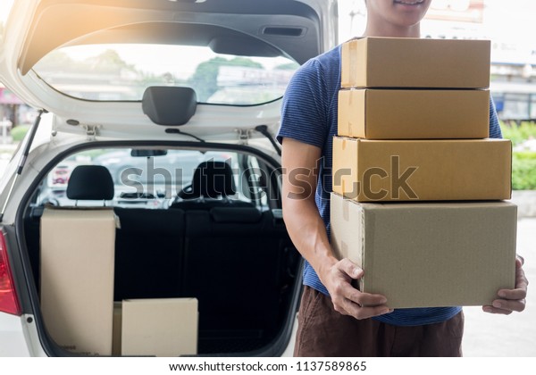 Delivery Loader Postman in blue uniform holding pile\
of cardboard box or carrying package while standing in front of a\
truck near van car