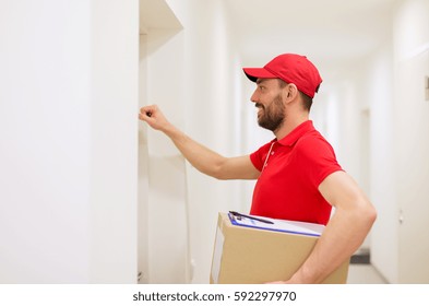 Delivery, Mail, People And Shipment Concept - Happy Man In Red Uniform With Parcel Box In Corridor Knocking On Door