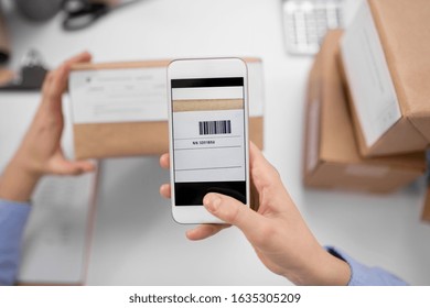 Delivery, Mail Service, People And Shipment Concept - Close Up Of Woman's Hands With Smartphone Scanning Barcode On Parcel Box At Post Office