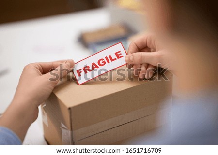 delivery, mail service, people and shipment concept - close up of woman sticking fragile mark to parcel box at post office