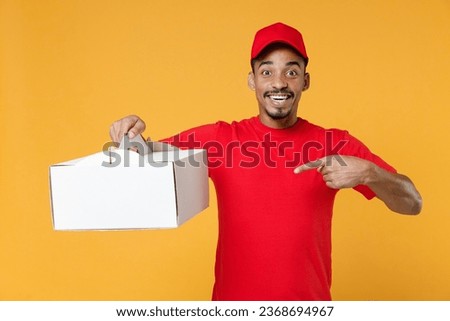 Delivery man of African American ethnicity wear red cap T-shirt work as dealer courier hold cake dessert in unmarked clear empty blank cardboard box isolated on plain yellow background studio portrait