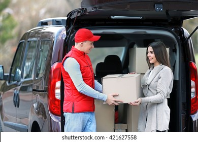 Delivery Man And Attractive Young Woman Receiving A Package, Near The Car Outdoors