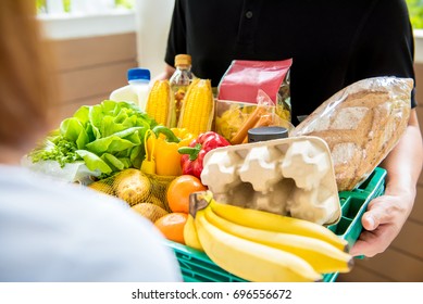 Delivery Man In Black Uniform Delivering Food To Customer At Home - Online Grocery Shopping Service Concept