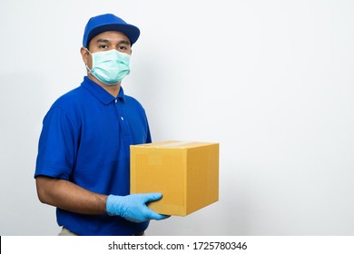 Delivery man blue uniform wearing rubber gloves and mask holding parcel cardboard box on white background.