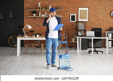 Delivery man with bottle of water talking by phone in office