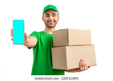 Delivery Man With A Box, Smartphone. Courier In Uniform Cap And T-shirt Service Fast Delivering Orders. Young Guy Holding A Cardboard Package. Character On Isolated White Background For Mockup Design