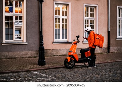  delivery man in a bright uniform on a moped picks up an order from a restaurant for quick delivery to a client. delivery man looks at the navigator in his phone - Powered by Shutterstock