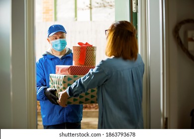 Delivery Man Bringing Holiday Packages. Woman At Home Standing In Doorway, Receiving Parcels For Christmas Gifts. Delivery Guy In Protective Mask And Gloves.