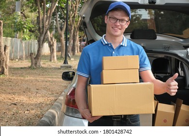 Delivery Man Carrying Packgage At Back Of Car. Male Postal Courier Person Deliver Cardboard Parcel Box