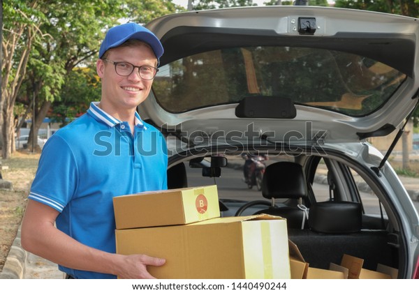 delivery man carrying\
packgage at back of car. male postal courier person deliver\
cardboard parcel box
