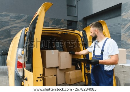 Delivery man checking inventory on a clipboard while inspecting cardboard boxes inside a yellow van parked on the street