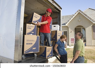 Delivery Man And Couple Unloading Moving Boxes From Truck Into New House