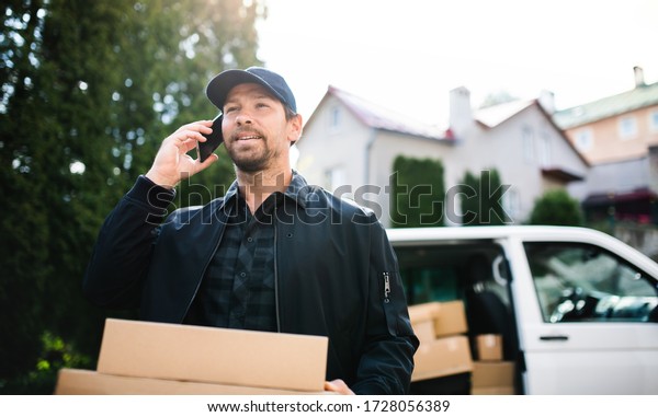 Delivery man courier delivering parcel box in\
town using smartphone.