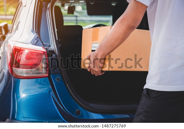 Delivery man is delivering cardboard box to\
customers via private car trunk door. People lifestyles and\
business occupation concept. Young male courier in casual clothes.\
Parcel move courier\
service