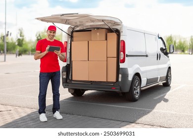 Delivery man driver checking his list of deliveries using digital tablet, standing near van outdoors, full length shot - Powered by Shutterstock