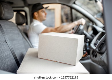 Delivery man driving cargo vehicle with parcels on the passenger seat, image focused on the cardboard boxes with blank space - Powered by Shutterstock