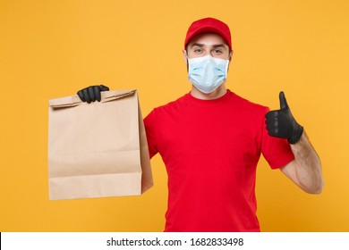 Delivery man employee in red cap t-shirt uniform mask glove hold craft paper packet with food isolated on yellow background studio Service quarantine pandemic coronavirus virus 2019-ncov concept