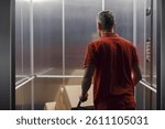 Delivery man getting in the elevator and pushing a hand truck loaded with boxes, back view